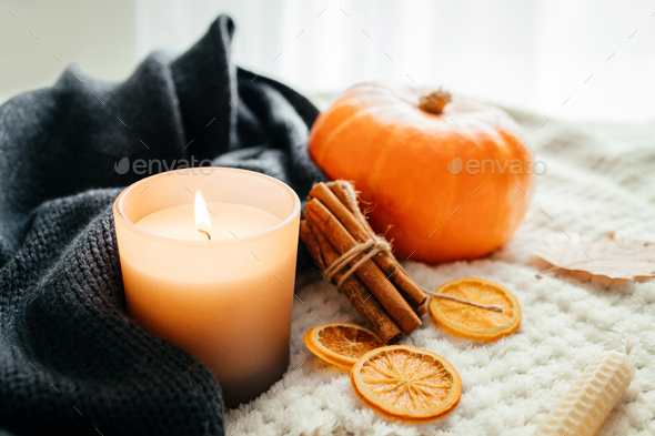 Autumn decor.A burning candle next to a knitted woolen sweater and a pot of hot tea.Atmospheric mood