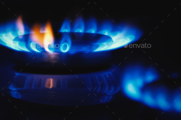 Gas stovetop cooker blue flame in the dark, gas rings burning, closeup