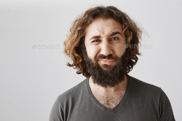 Man is not sure, having doubt. Portrait of attractive curly-haired husband frowning and grimacing