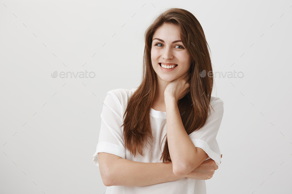 Portrait of cute ordinary caucasian girl feeling insecure or uncomfortable, smiling and touching