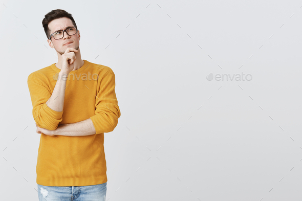 Hmm what if. Smart and thoughtful good-looking guy in geek glasses and cozy yellow sweater holding