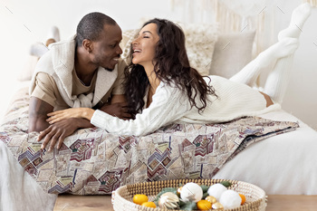 A couple in love - a black man and a mulatto woman on a bed in a bright room. Diverse family