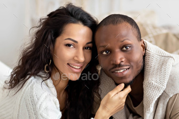 A couple in love - a black man and a mulatto woman on a bed in a bright room. Diverse family