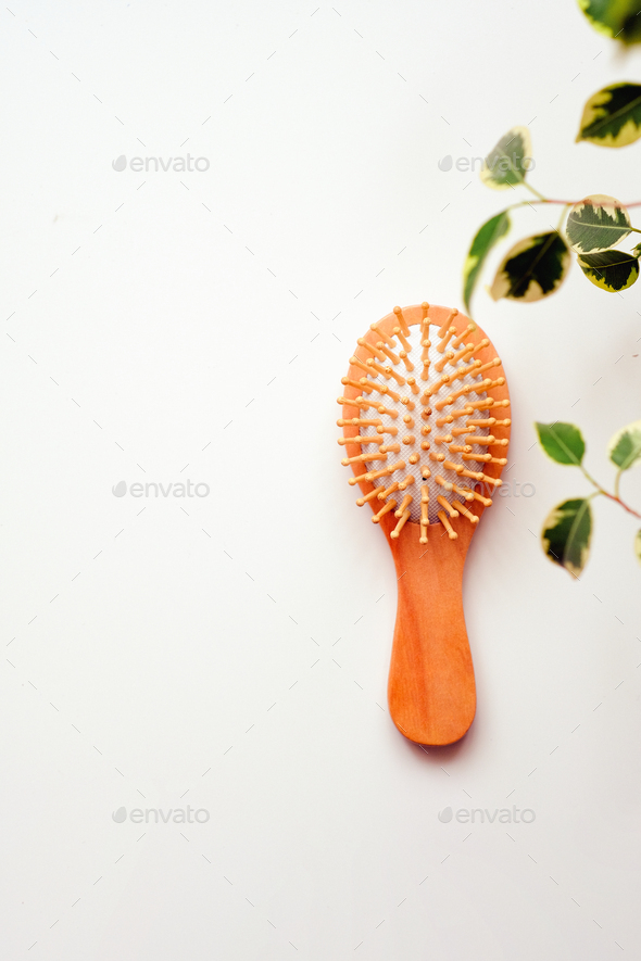 Small round wooden natural hair comb on a white table. Ficus greenery in the frame. Hair care.