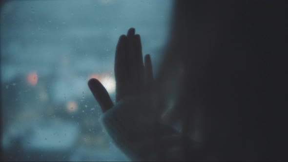 Hand of a woman touching a window in a rainy day alt