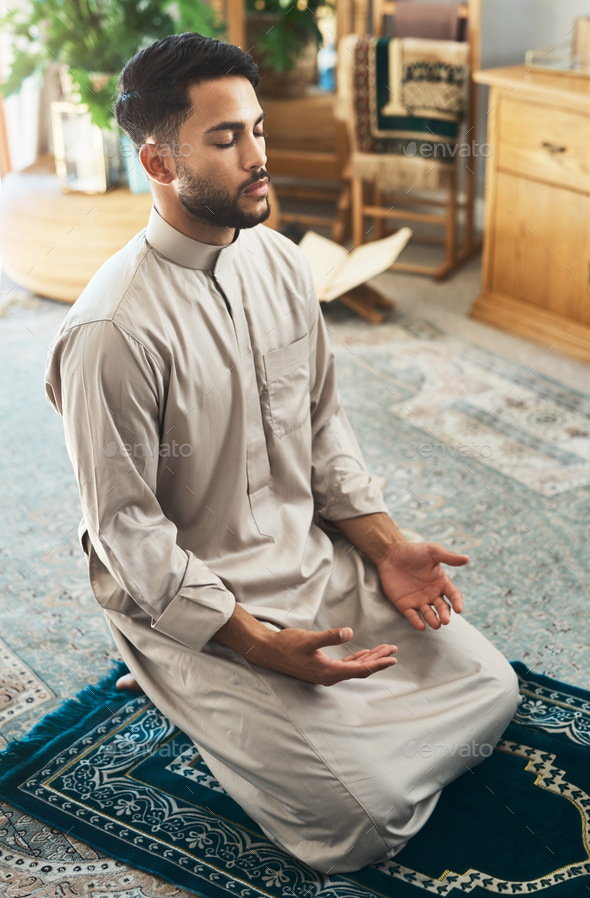 Find yourself a quiet place. Shot of a young muslim man praying in the lounge at home.