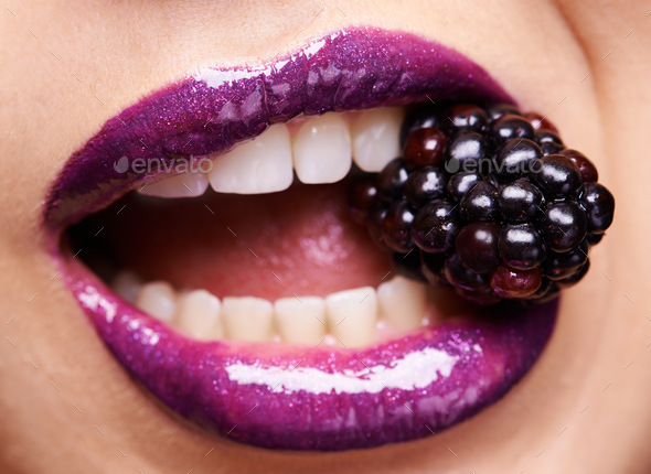 Indulging in forbidden fruit. Shot of a woman wearing purple lipstick and biting into a blackberry.