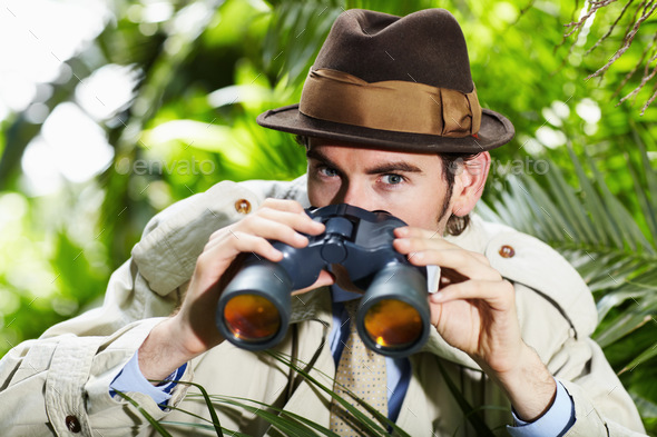 He doesnt miss a thing. Private investigator using binoculars to spy on someone from the bushes.