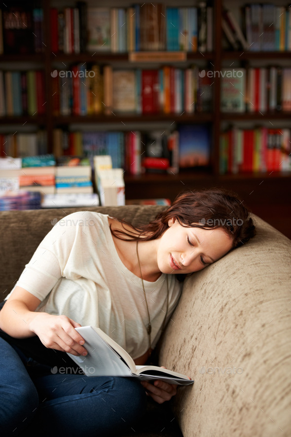 Spirited away with words. An attractive young woman relaxing on a sofa with a book.