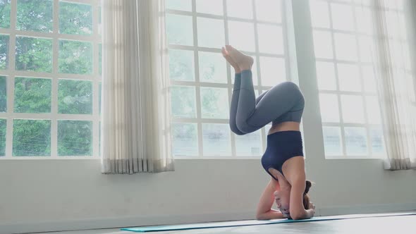 Young Asian sporty woman practicing yoga on mat in headstand pose