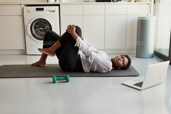 Am I doing this right. Shot of a young woman using a laptop while exercising at home.