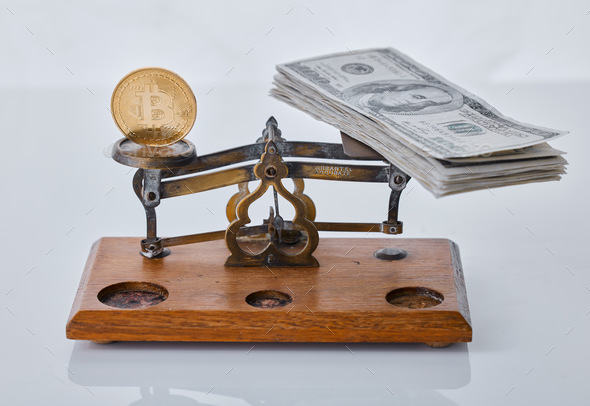 Shot of a scale balancing a coin and a wad of cash against a grey background