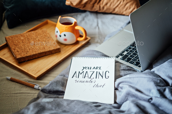 Positive daily affirmations for self love. Words You Are Amazing in notebook near laptop and tea