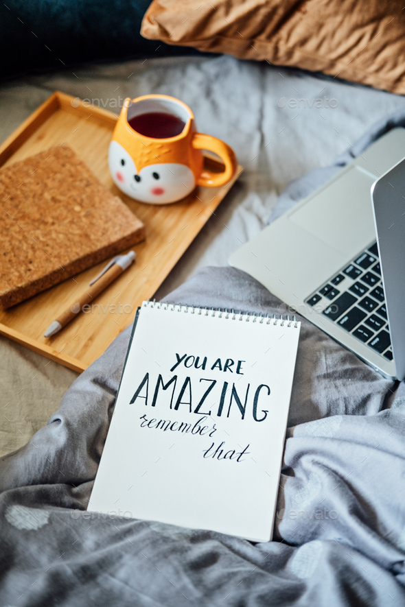 Positive daily affirmations for self love. Words You Are Amazing in notebook near laptop and tea