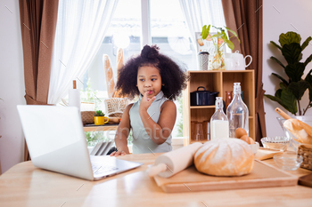 Happy African American girl use laptop and having fun while preparing cookie dough at home.