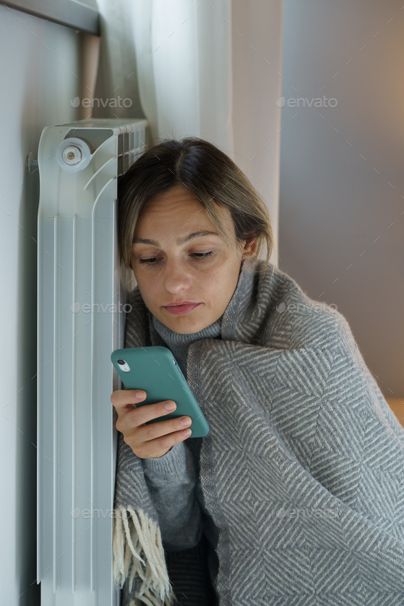 Upset woman leaning on heating radiator searches vacancy for applying for job scrolling smartphone