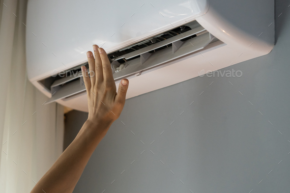 Owner of apartment tries to warm room reaching hand to operating air conditioner on grey wall