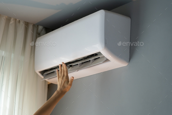 Owner of apartment tries to warm room reaching hand to operating air conditioner on grey wall