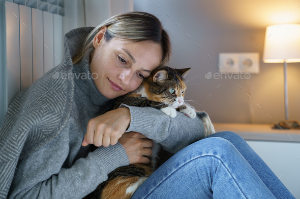 Young woman covered with warm blanket feels better hugging domestic cat and tries to continue life