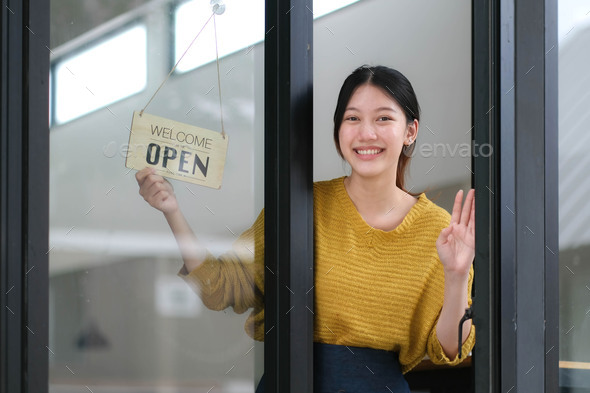 Young Asia manager girl changing a sign from closed to open sign on door cafe looking outside
