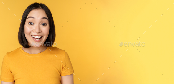 Close up portrait of asian girl showing surprised reaction, raising eyebrows amazed, reacting to