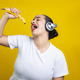 Latin woman singing with banana and wearing headphones, in yellow background - PhotoDune Item for Sale