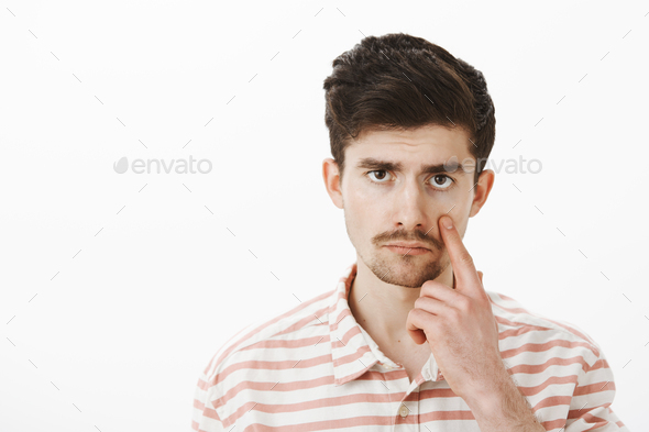 Unimpressed with boring conversation. Displeased bored guy in casual striped shirt, pulling eye and