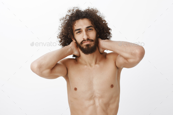 Waist-up shot of confident beautiful hispanic bearded guy with curly hair, holding hands behind neck