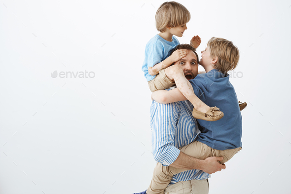 Kids fooling around with cool dad. Portrait of playful happy sons hanging on father body, having fun