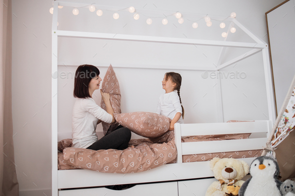Overjoyed young mom and happy little daughter have fun engaged in pillow fight in bedroom