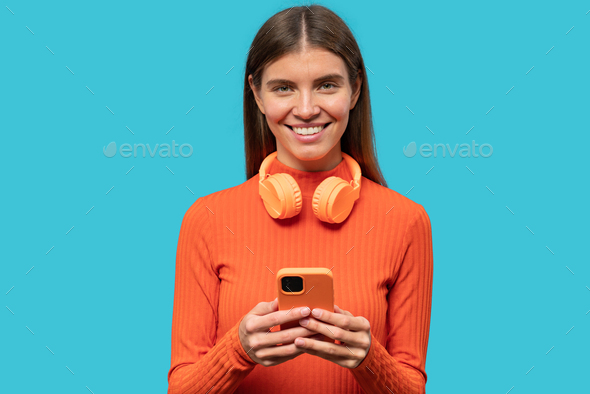 Woman with headphones around neck creating playlist in music app on phone on blue background