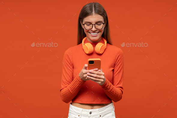 Woman in glasses wearing headphones around neck using phone app to download music - Stock Photo - Images