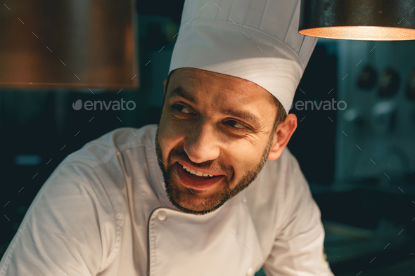 Close up of smiling male chef in uniform standing on kitchen of restaurant and looking - Stock Photo - Images