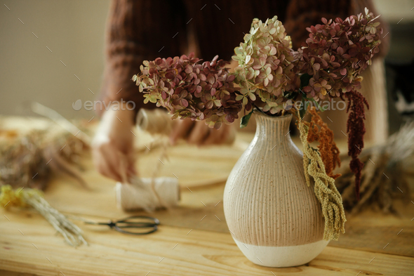 Dried hydrangea flowers in vase on background of woman arranging