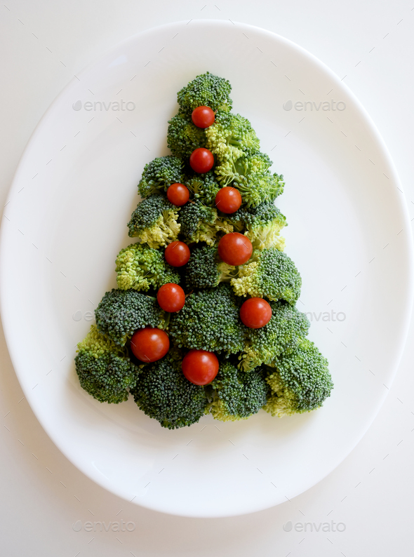 Christmas Tree made of broccoli and small tomatoes on white plate on white background.