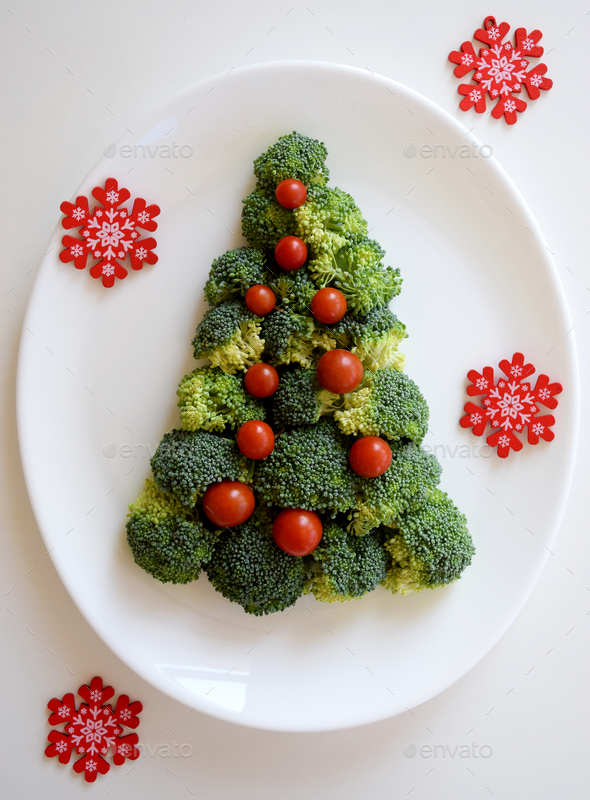 Christmas Tree made of broccoli and small tomatoes on white plate on white background.