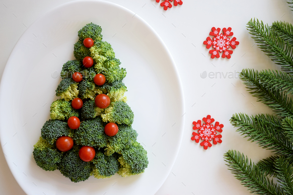 Christmas Tree made of broccoli and small tomatoes on white plate with red snowflakes and fir tree