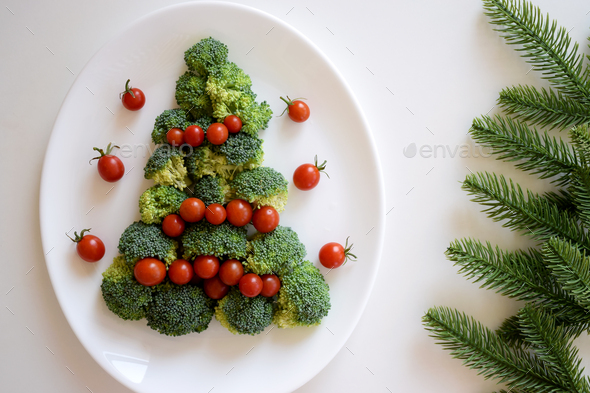 Christmas Tree made of broccoli and small tomatoes on white plate with fir tree