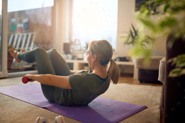 Athletic woman using hand weights while doing sit-ups in the living room.