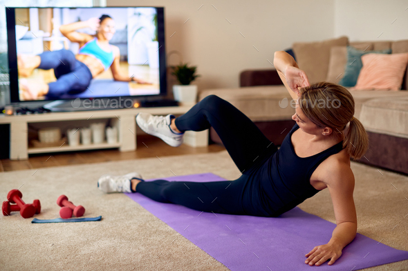 Athletic woman doing side sit-ups while exercising in front of a TV at home.