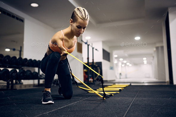 Disabled athletic woman using feet agility ladder during sports training in a gym.
