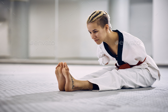 Young athletic woman with para-ability stretching on floor during taekwondo training in health club