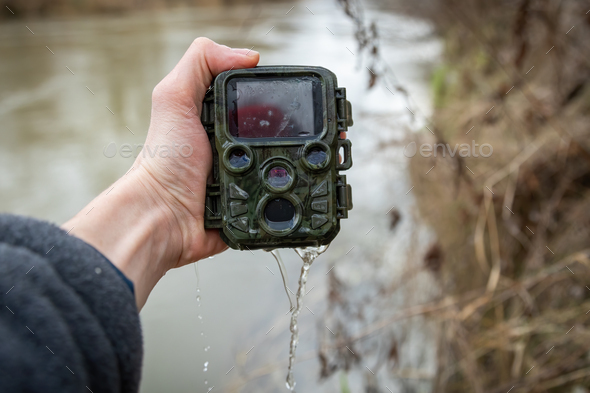 Hand holding a drowned trail camera near river with water leaking in.
