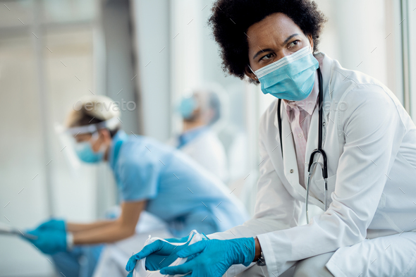 Distraught African American female doctor with protective face mask at hospital hallway.