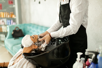 Young woman with protective face mask enjoying during hair wash at hairdresser's.