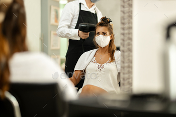 Woman with protective face mask getting her hair styled at hairdresser during virus epidemic.