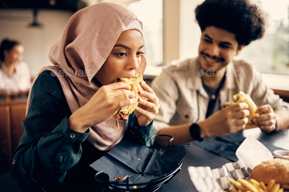 Young Muslim woman eating with friends on lunch break in cafeteria.