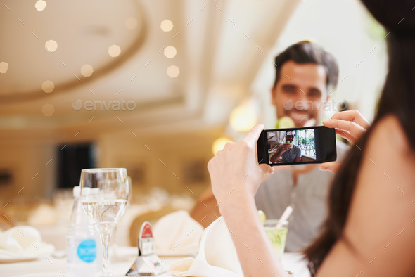 A woman taking a picture of her partner while dining out at a fancy restaurant