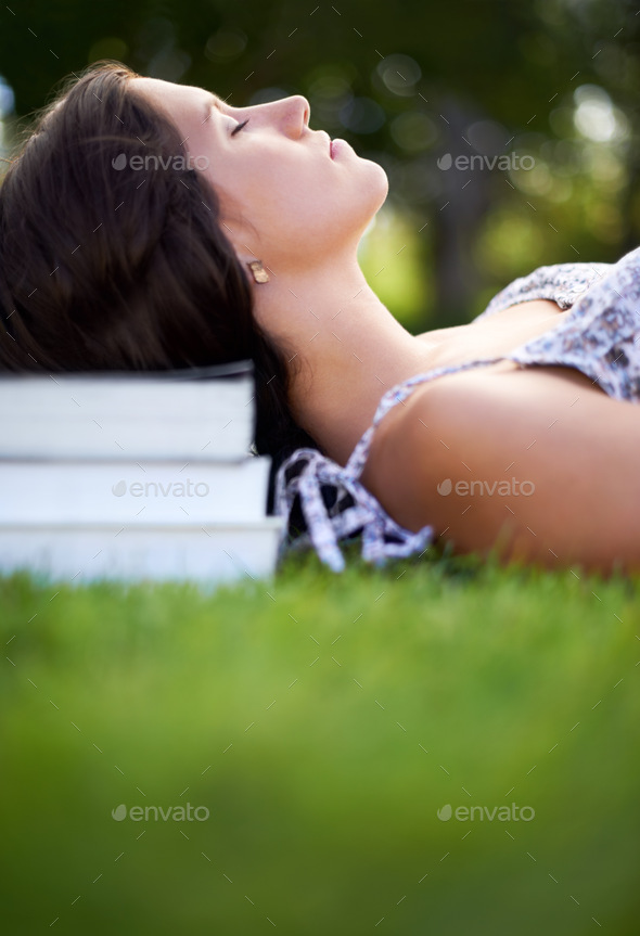 Let your mind wander...A young woman lying in a park with her head resting on a pile of books.
