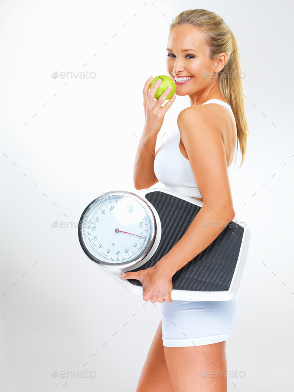 Living well through diet and exercise. Shot of a young woman holding a scale and eating an apple.